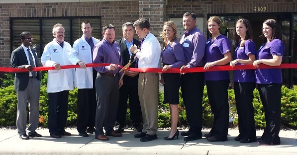 a group of people standing in front of a building cutting a red ribbon