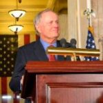 man in a dark suit speaks at a podium