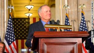 man in a dark suit speaks at a podium
