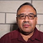 Man with glasses looking at the camera in front of a stone wall