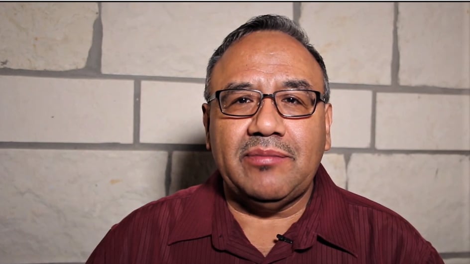 Man with glasses looking at the camera in front of a stone wall
